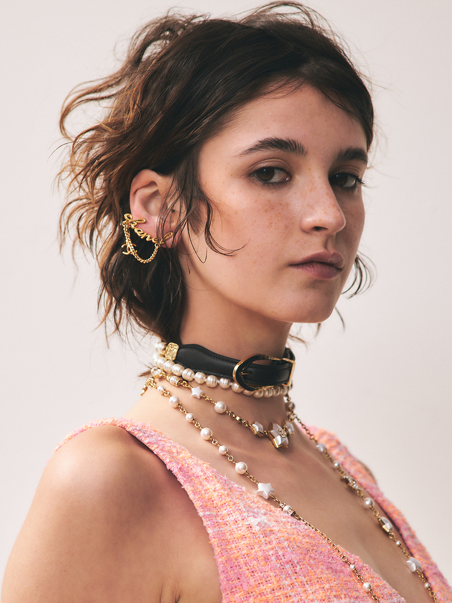 Close up portrait of a model with natural makeup and many gold and pearl accessories making eye contact with the camera 